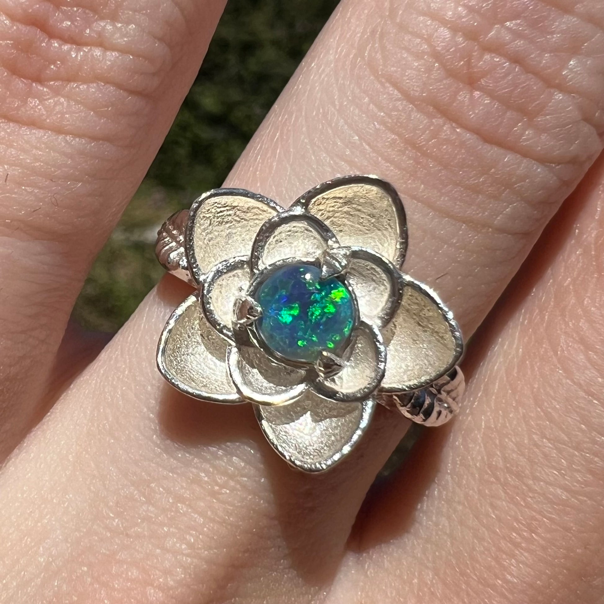 Close-up of women's black opal ring with sterling silver lotus flower motif, worn on finger in sunlight