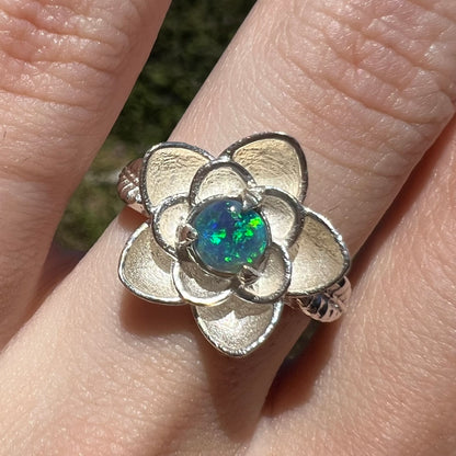 Close-up of women's black opal ring with sterling silver lotus flower motif, worn on finger in sunlight