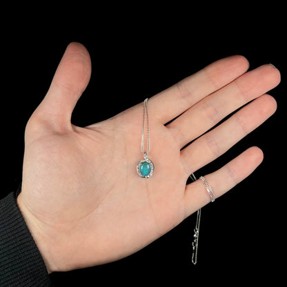 Hand holding women's platinum black opal necklace under cool LED studio light.  The opal has a pearlescent blue iridescence.