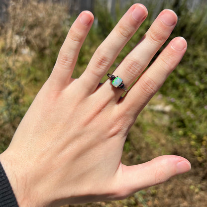 Hand wearing women's black rhodium-plated sterling silver ring set with three Ethiopian opals in natural sunlight