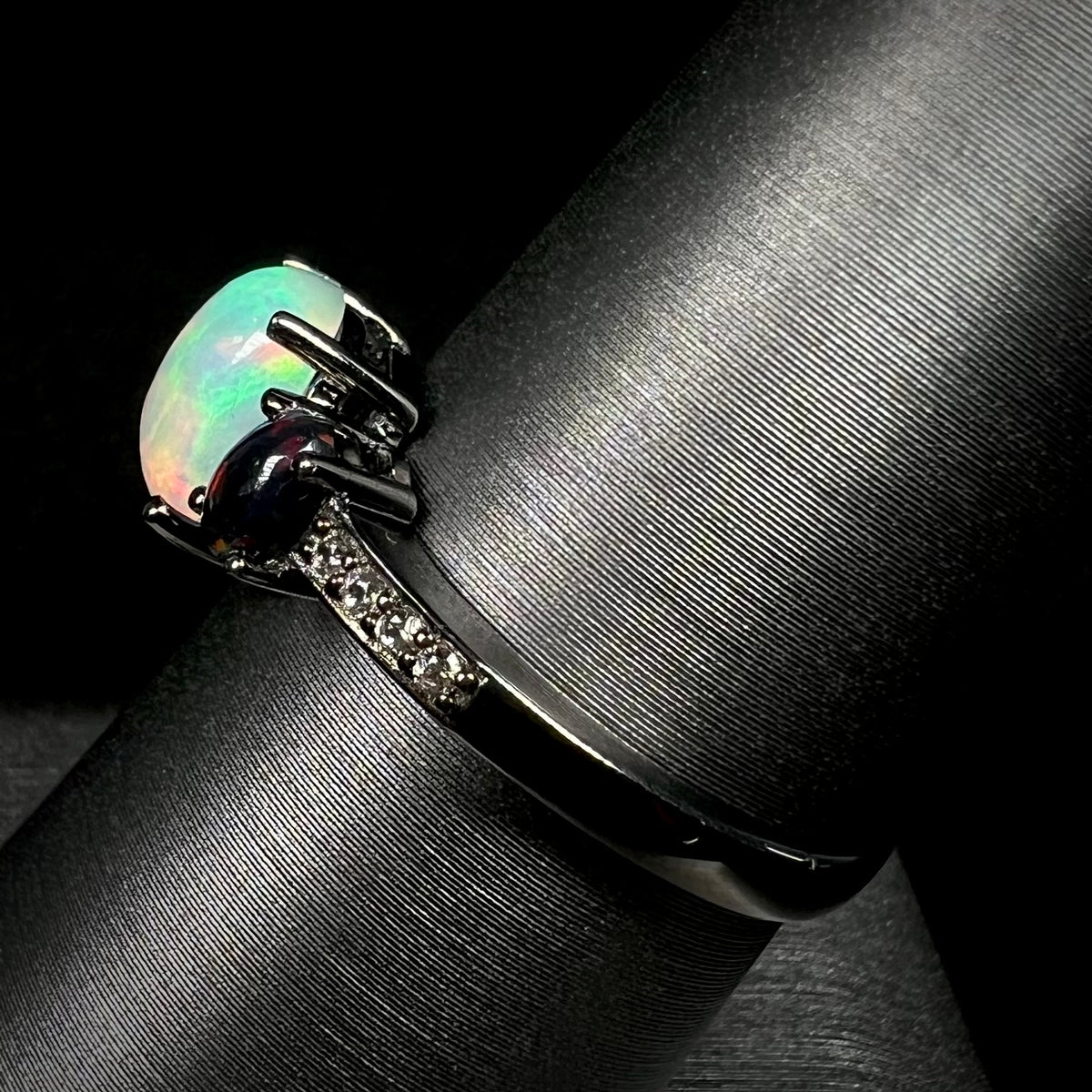 Side view of women's black rhodium plated sterling silver opal ring on display, focused on ring's CZ-accented black shank