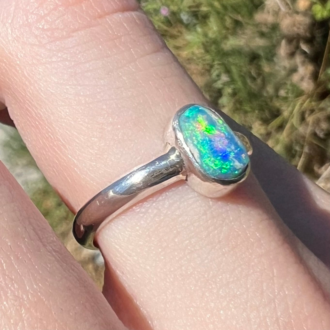 Blue and green flashes seen in women's silver Australian crystal opal ring in sunlight, worn on finger