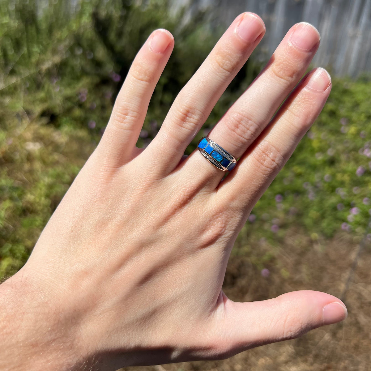 Sunlit hand wearing a women's five-stone blue Australian opal inlay ring, accented by two rows of channel-set diamonds in 14k white gold