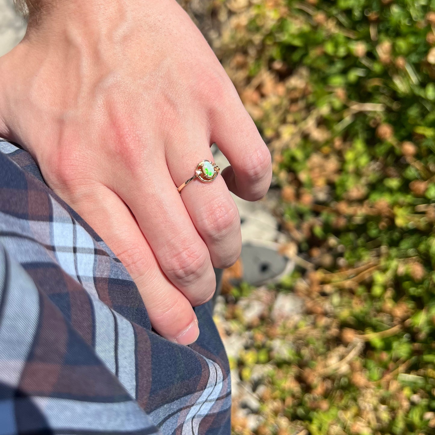 Close-up of a hand resting on a person's hip while wearing a dainty women's Australian opal ring.  The opal is green in natural light.