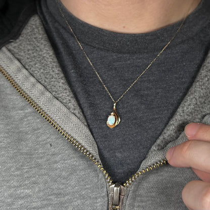 Close-up of person's neck and chest wearing women's dainty 14k gold opal and diamond necklace against dark shirt
