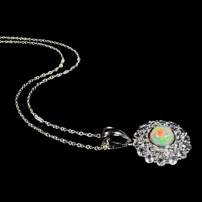 Angled view of a women's Ethiopian fire opal and tanzanite double-halo necklace laying on a black background, its silver chain flowing behind it.