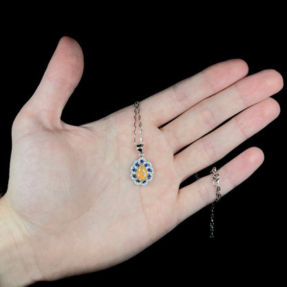 Women's Ethiopian opal, blue sapphire, and cubic zirconia necklace, held in hand; the chain is wrapped around pinky finger
