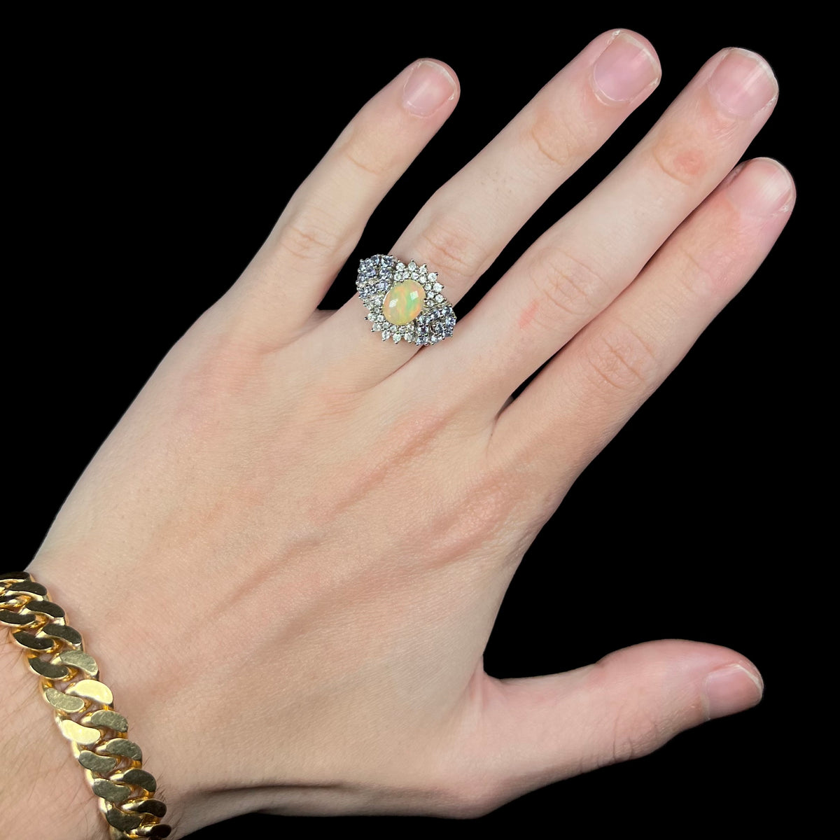 Hand wearing women's silver Ethiopian opal ring with clustered white topaz and blue tanzanite accent gemstone design