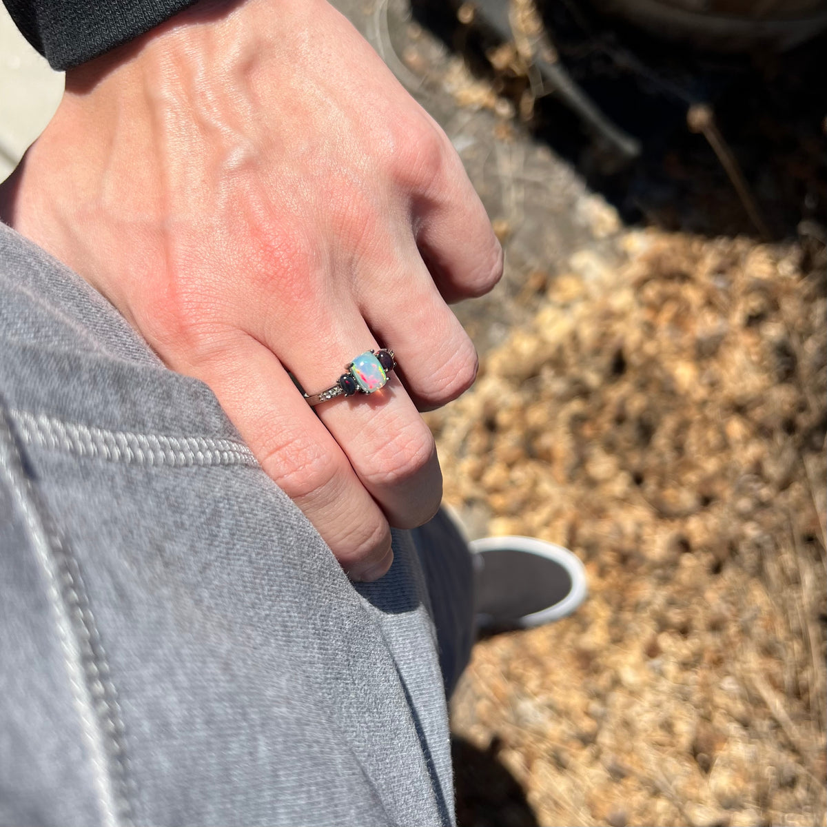 Person's hand resting on hip in sunlight wearing women's three-stone Ethiopian opal and CZ ring with black rhodium finish