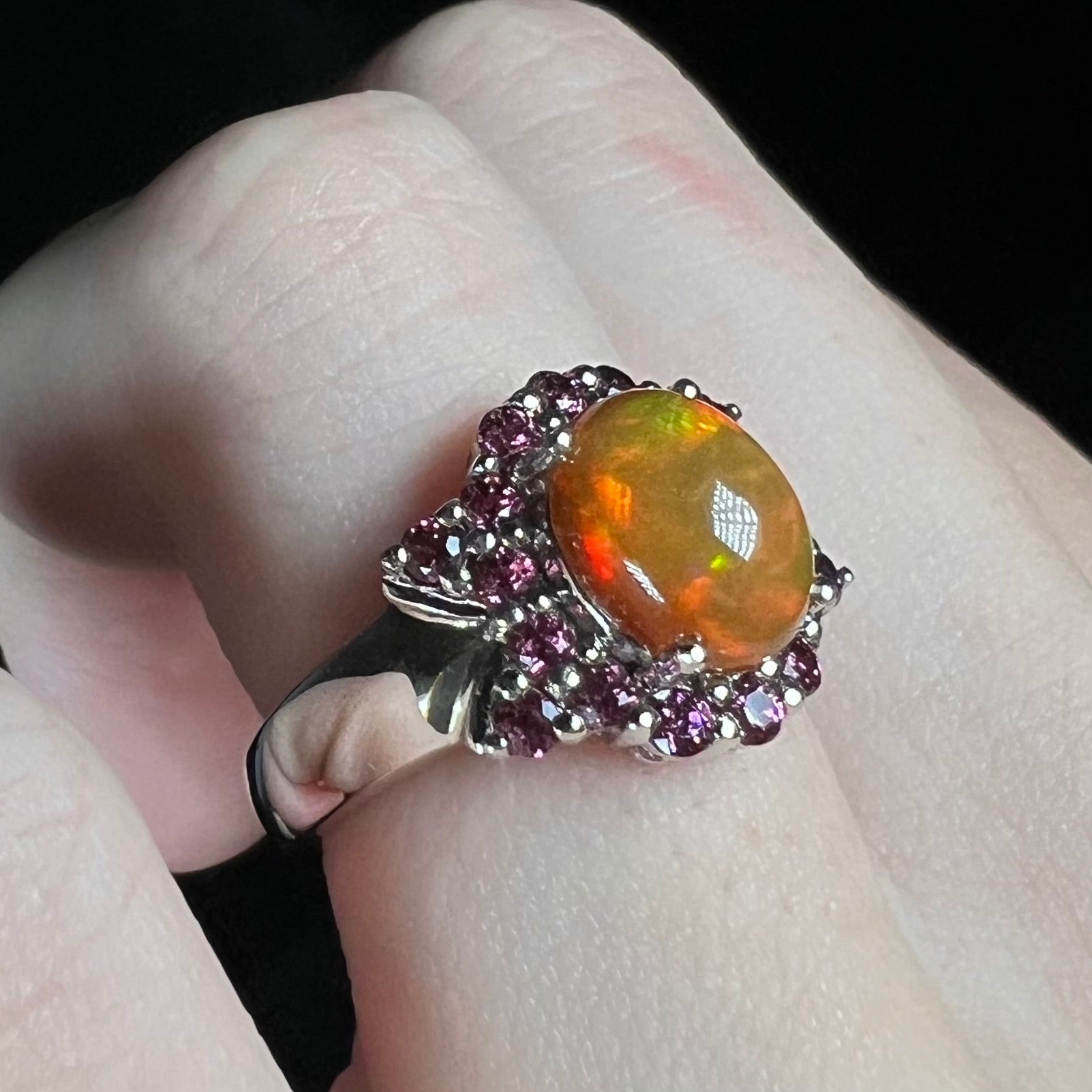 Women's Ethiopian opal and purple garnet ring, viewed from angle on finger under cool LED studio light