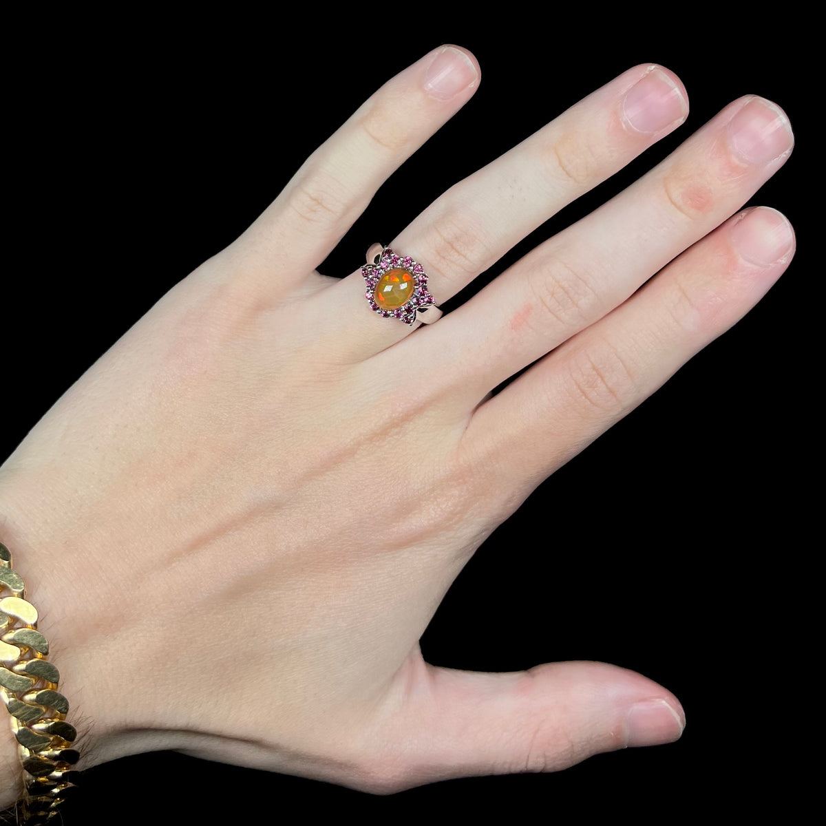Hand wearing women's silver Ethiopian opal ring with bowtie-shaped garnet halo design