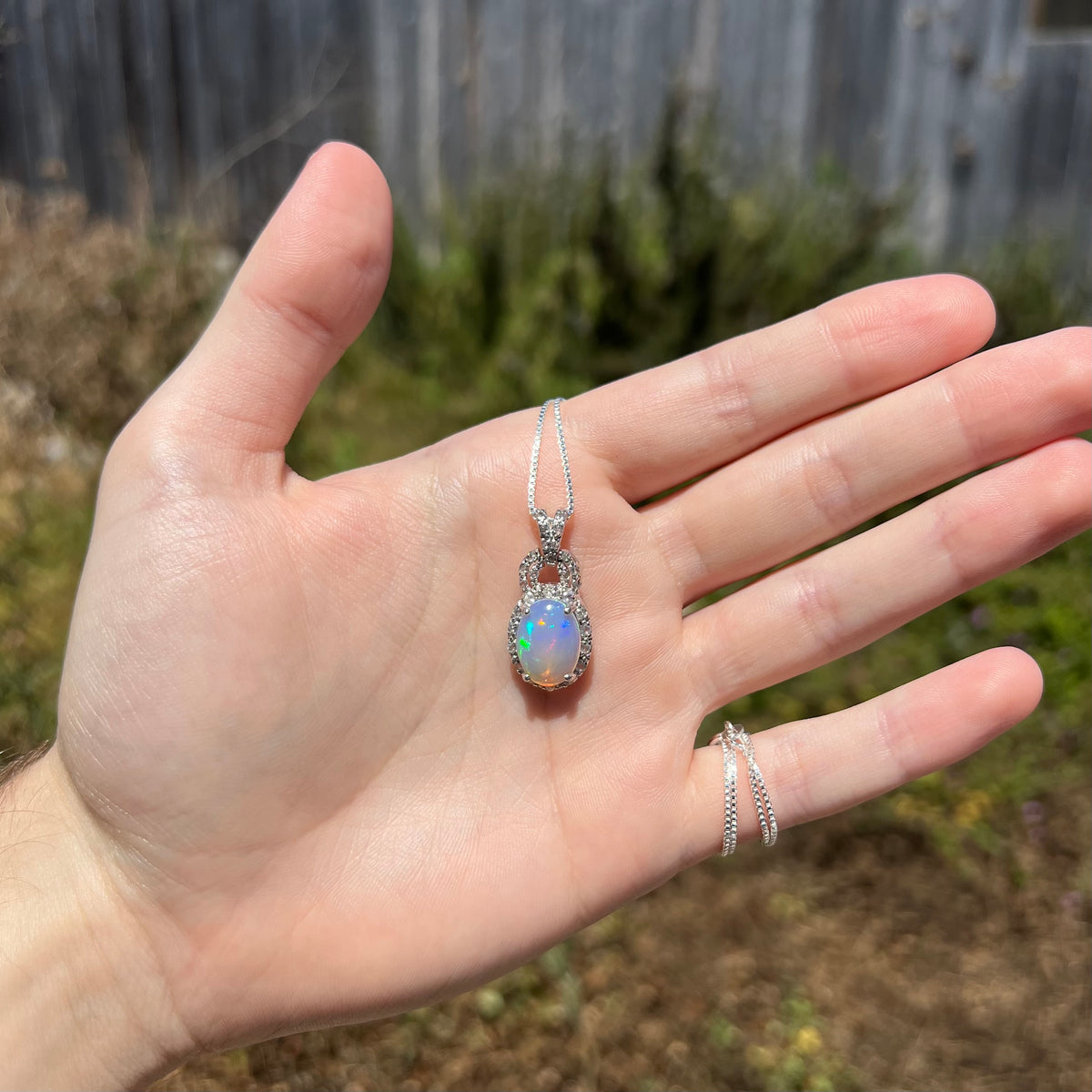 Hand holding women's sterling silver Ethiopian opal necklace in natural sunlight