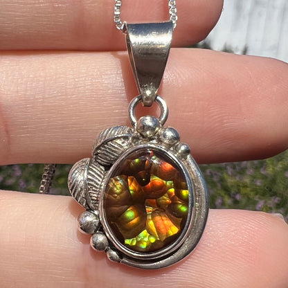 Close-up of women's fire agate pendant with Southwest-inspired sterling silver design, held in hand under natural sunlight.