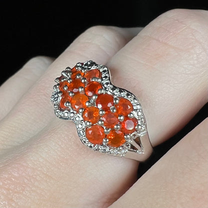 A women's sterling silver Mexican fire opal cluster ring with a filigree design, worn on a finger and shown close-up from an angle.