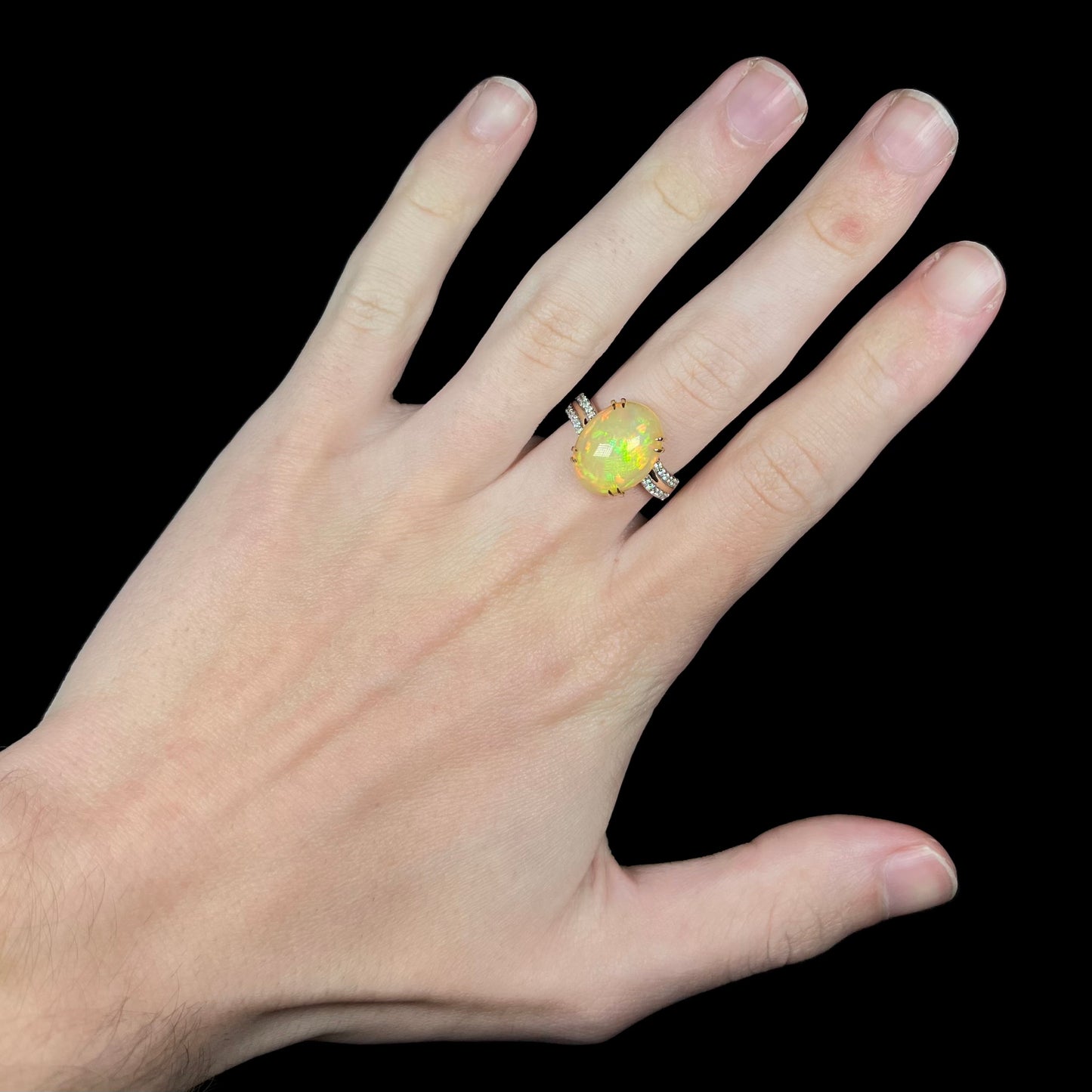 Hand wearing women's Ethiopian fire opal and diamond cocktail ring in 14k gold with delicate split-prong design