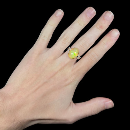 Hand wearing women's Ethiopian fire opal and diamond cocktail ring in 14k gold with delicate split-prong design