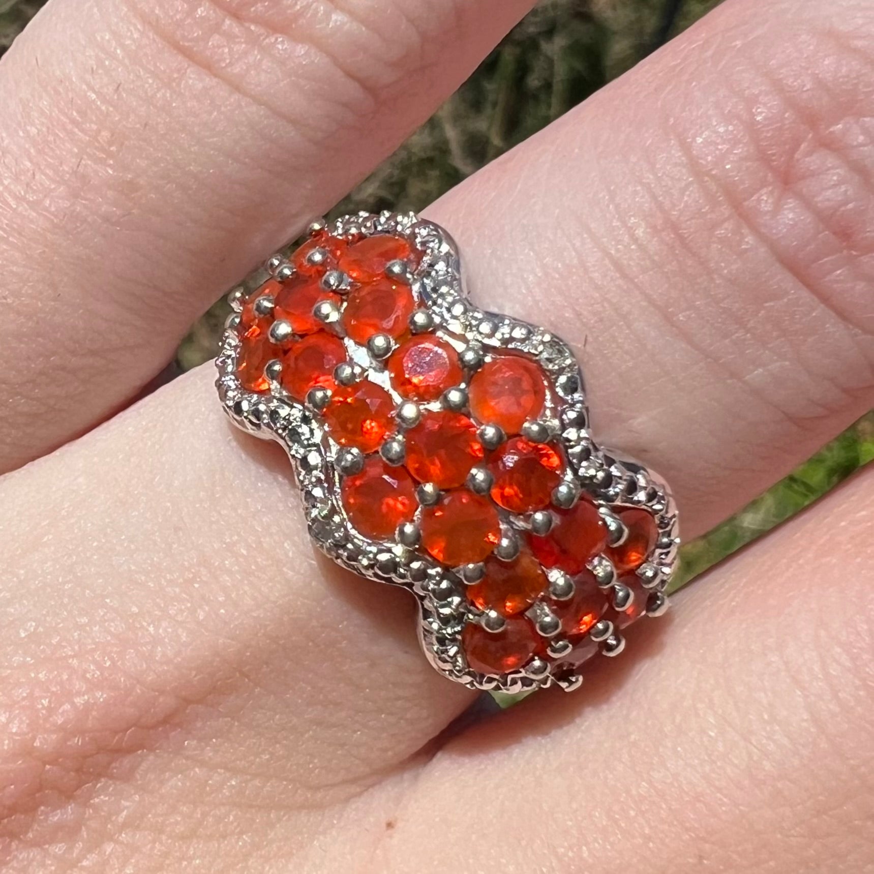 Close-up macro view of a women's sterling silver Mexican fire opal and diamond ring in natural sunlight, worn on a finger.