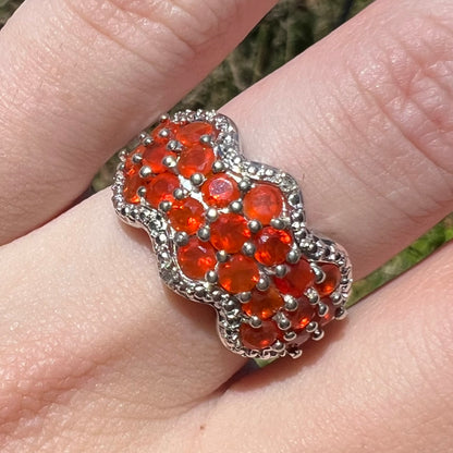 Close-up macro view of a women's sterling silver Mexican fire opal and diamond ring in natural sunlight, worn on a finger.