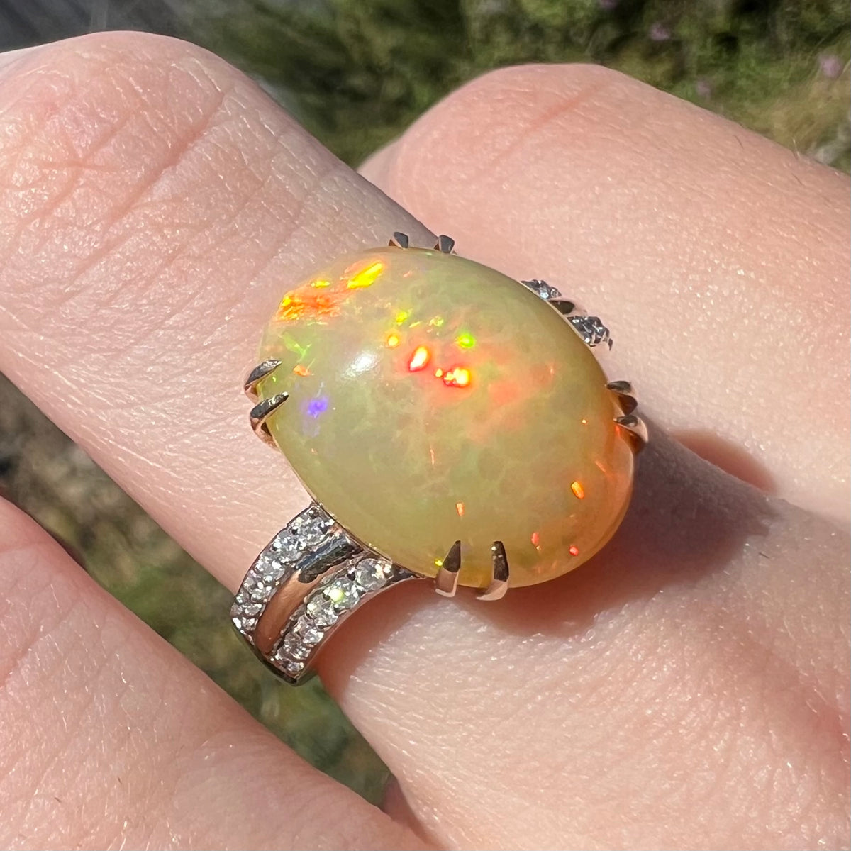 Women's fire opal and diamond ring with split-prong design shown close-up on finger in sunlight