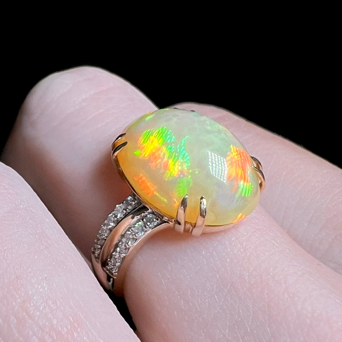 Women's 14k gold Ethiopian fire opal ring with diamond accents, shown close-up on finger.  Opal has green, red, yellow, and blue flashes of color