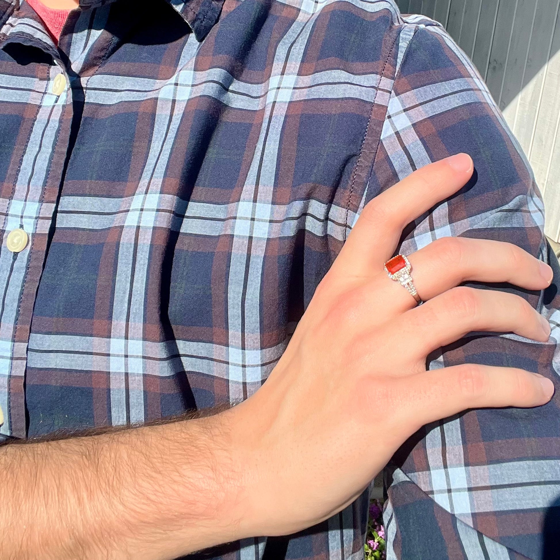 Hand resting on person's shoulder wearing a women's Mexican fire opal and white zircon ring in sunlight.  The person wears a blue plaid shirt.