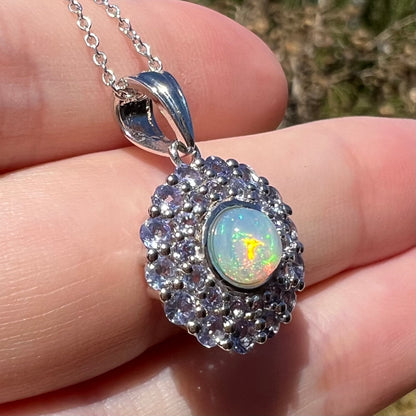 Orange and green flashes seen in a sterling silver women's fire opal and tanzanite halo pendant, shown from an angled close-up view in natural light.