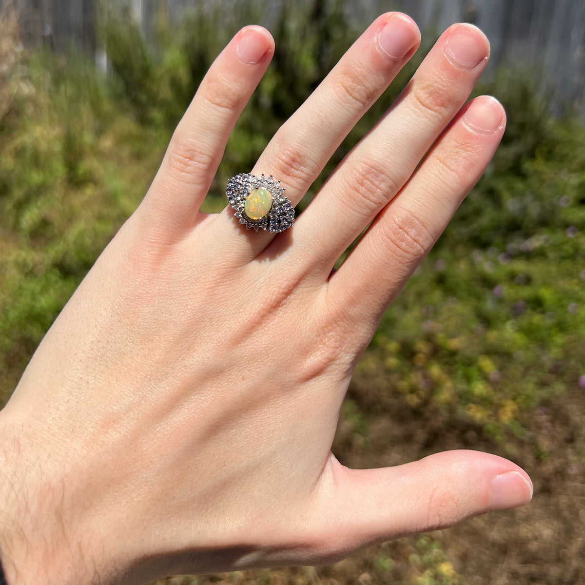 Women's silver fire opal ring with white topaz and tanzanite accents, worn on hand in sunlight