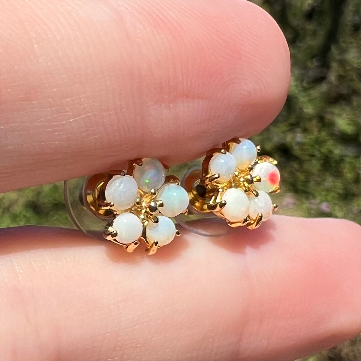 Pair of women's flower opal stud earrings shown between two fingers in natural light