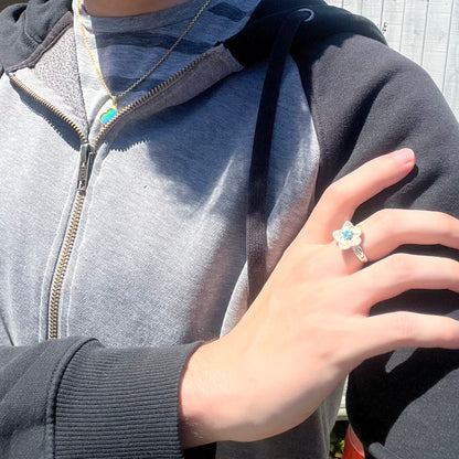 Close-up of person resting hand on shoulder in sunlight while wearing a women's silver flower ring set with a black opal