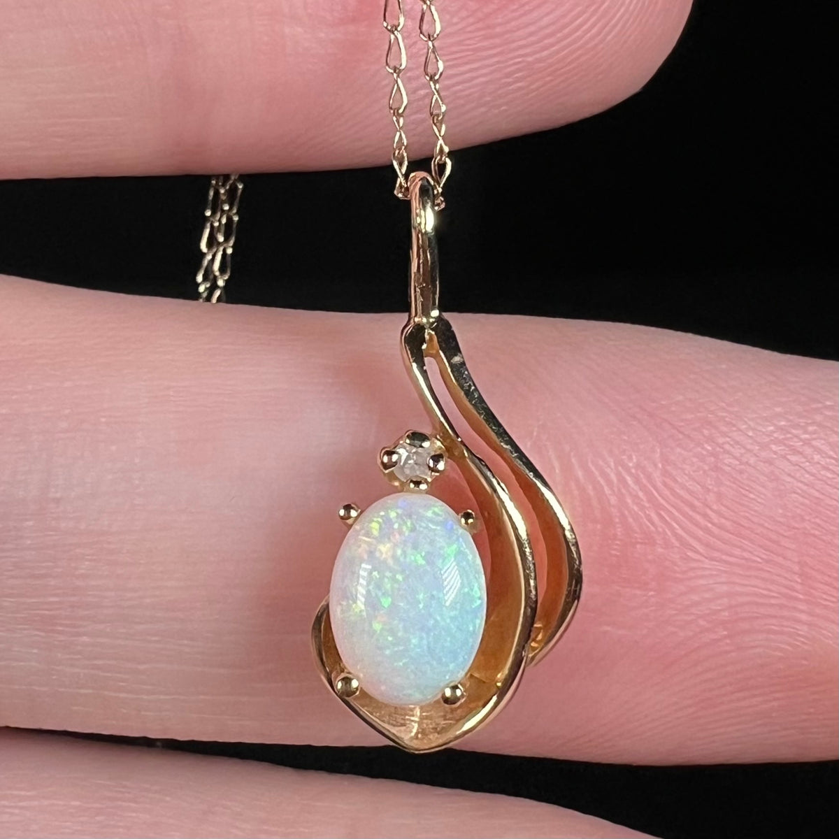 Close-up of women's 14k gold Modernist-style opal and diamond pendant, held on top of fingers with chain