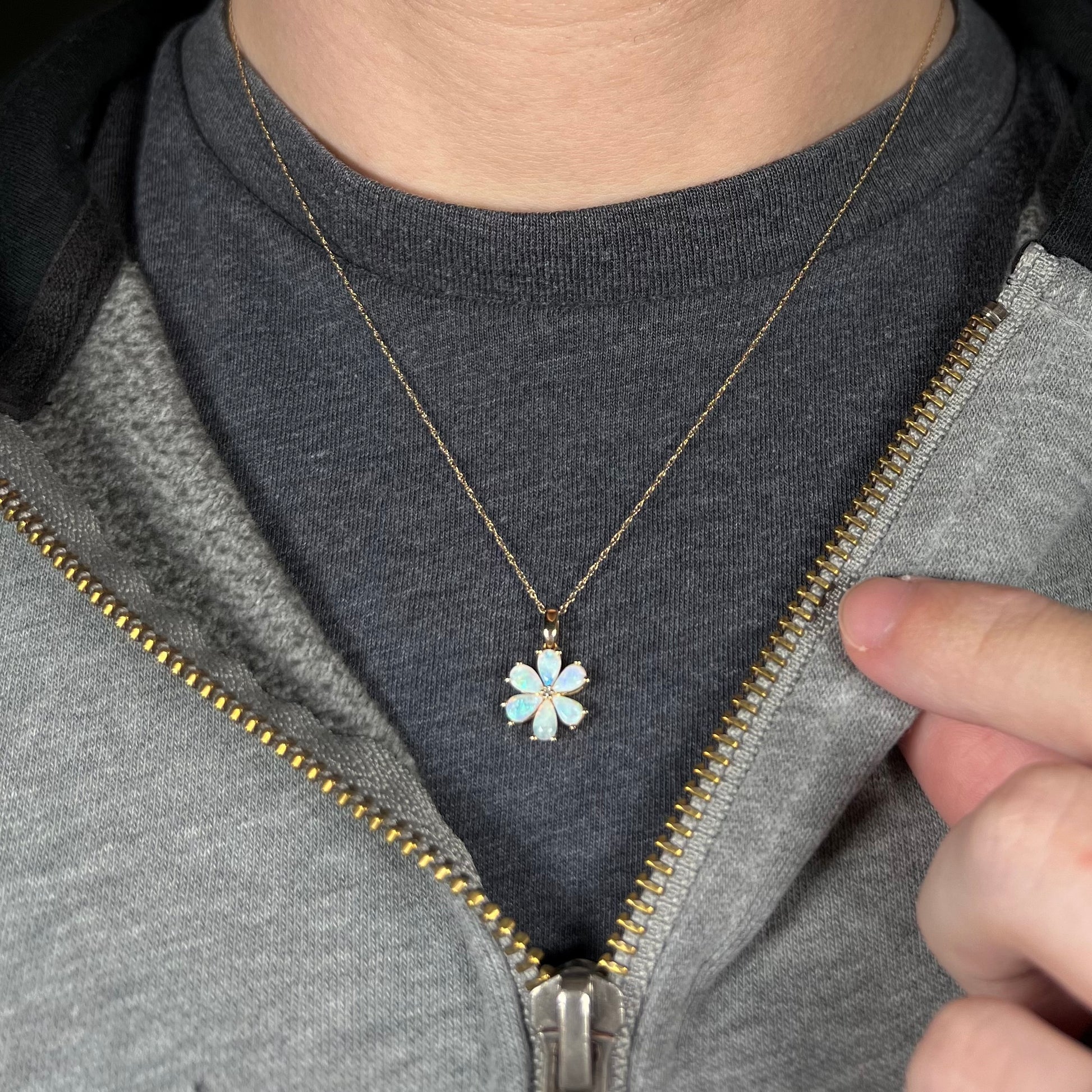 Close-up of person wearing women's gold opal flower necklace around neck against dark shirt