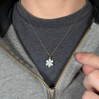 Close-up of person wearing women's gold opal flower necklace around neck against dark shirt