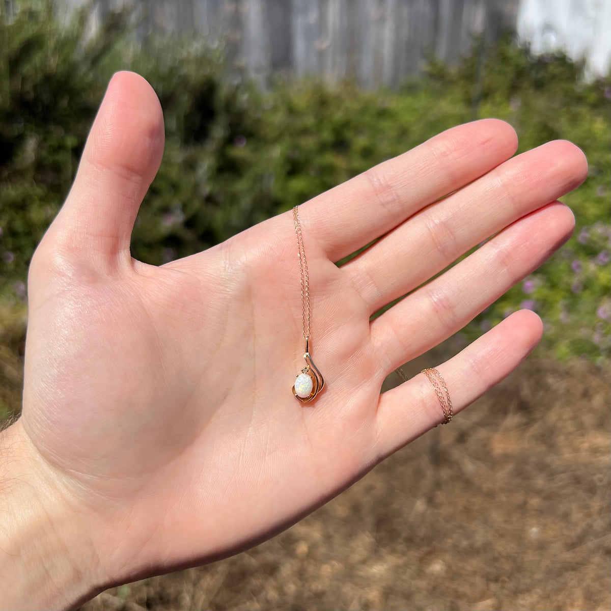 Women's 14k gold natural opal and diamond necklace held in hand under sunlight