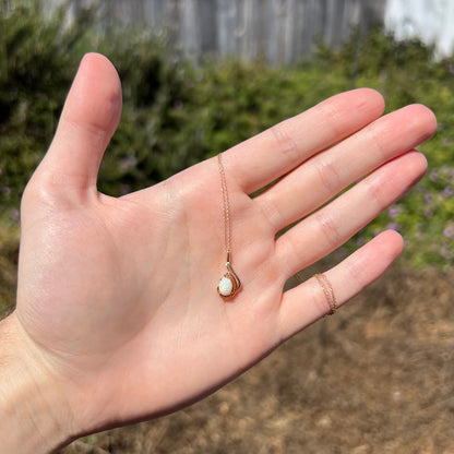 Women's 14k gold natural opal and diamond necklace held in hand under sunlight