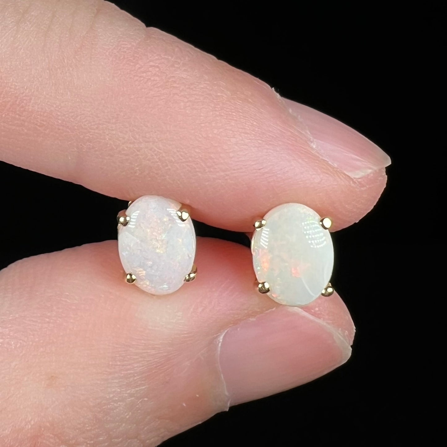 Women's gold opal stud earrings up-close in fingers