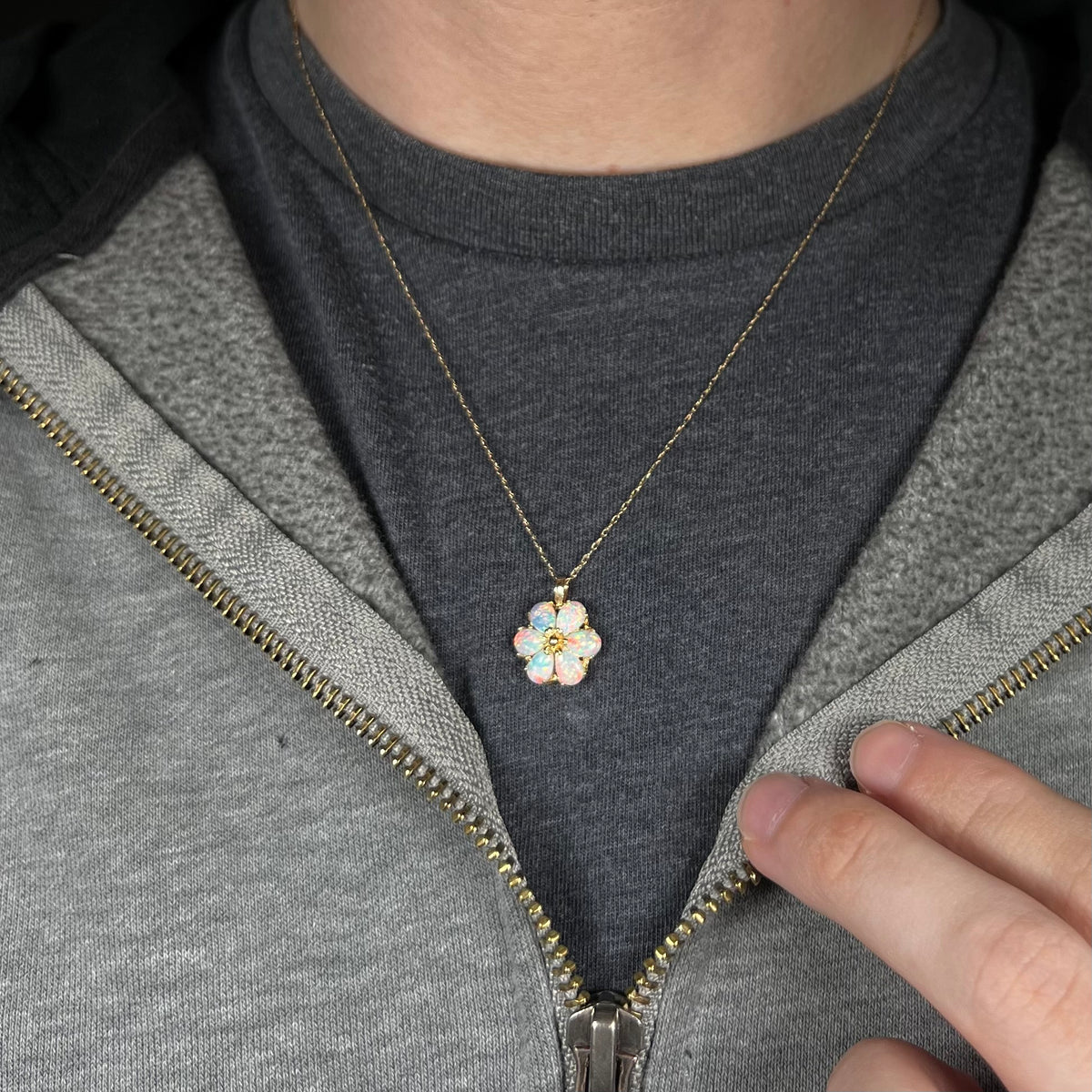 Close-up of person's neck and chest wearing women's 14k gold synthetic opal flower necklace against a dark shirt