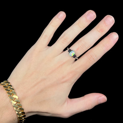 Hand wearing women's gothic style three-stone Ethiopian opal ring with black rhodium finish
