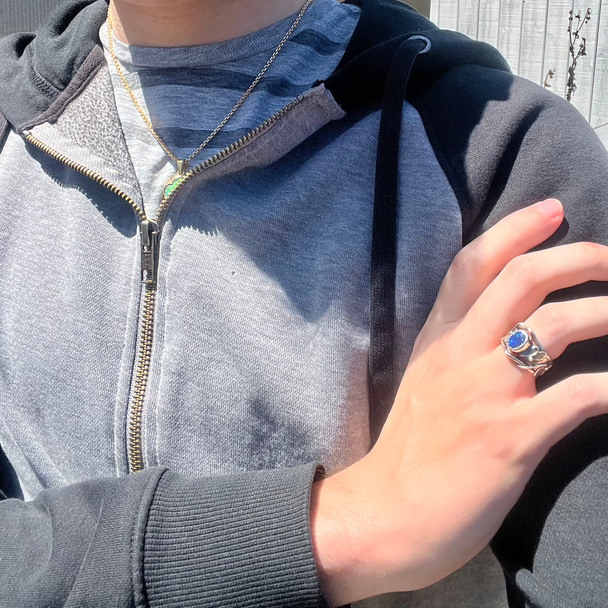 Close-up of person resting hand on opposing shoulder wearing women's handmade sterling silver black opal doublet ring with twisting vine design in sunlight