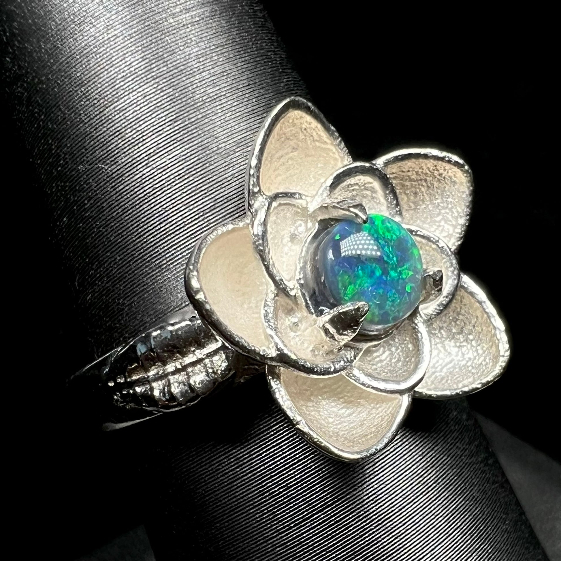 Angled close-up of women's silver lotus flower ring set with black opal, shown on ring display