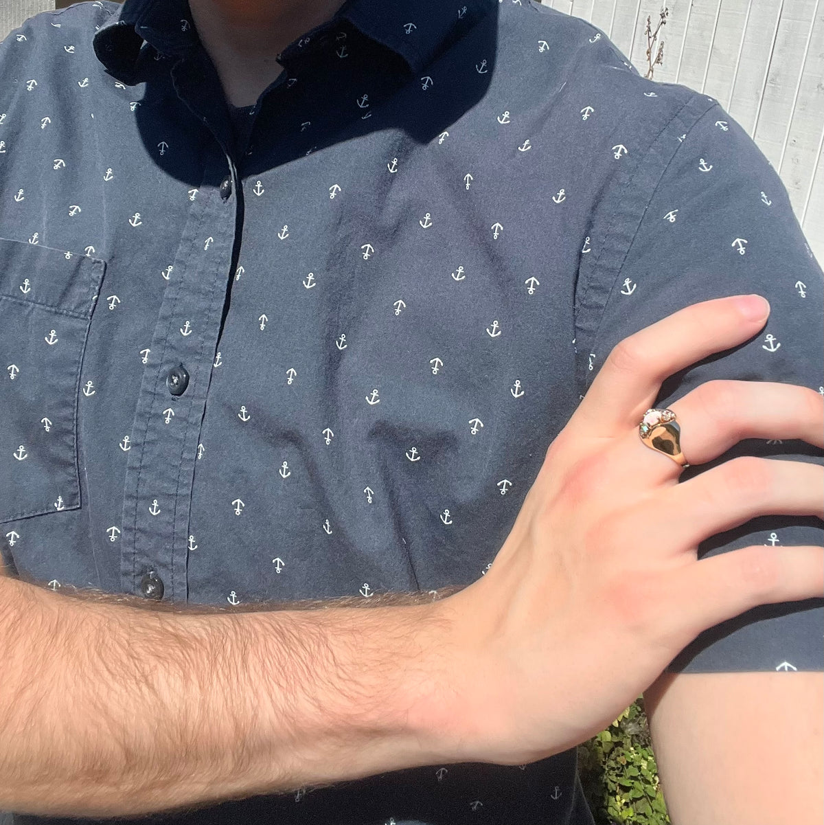 Close-up of person resting hand on opposing shoulder in sunlight wearing a women's Mid-Century 14k gold opal and diamond ring with domed design