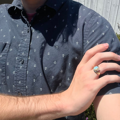 Close-up of person resting hand on opposing shoulder in sunlight while wearing women's Modernist style gold opal and diamond ring