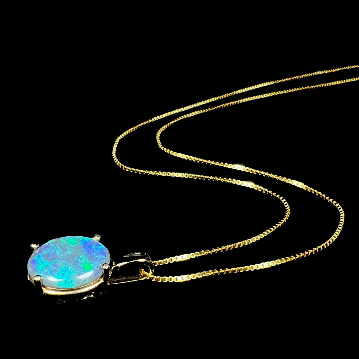 Women's natural black opal necklace in gold-tone metal with 14k pendant setting shown from angle laying on black background, its chain flowing