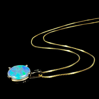 Women's natural black opal necklace in gold-tone metal with 14k pendant setting shown from angle laying on black background, its chain flowing