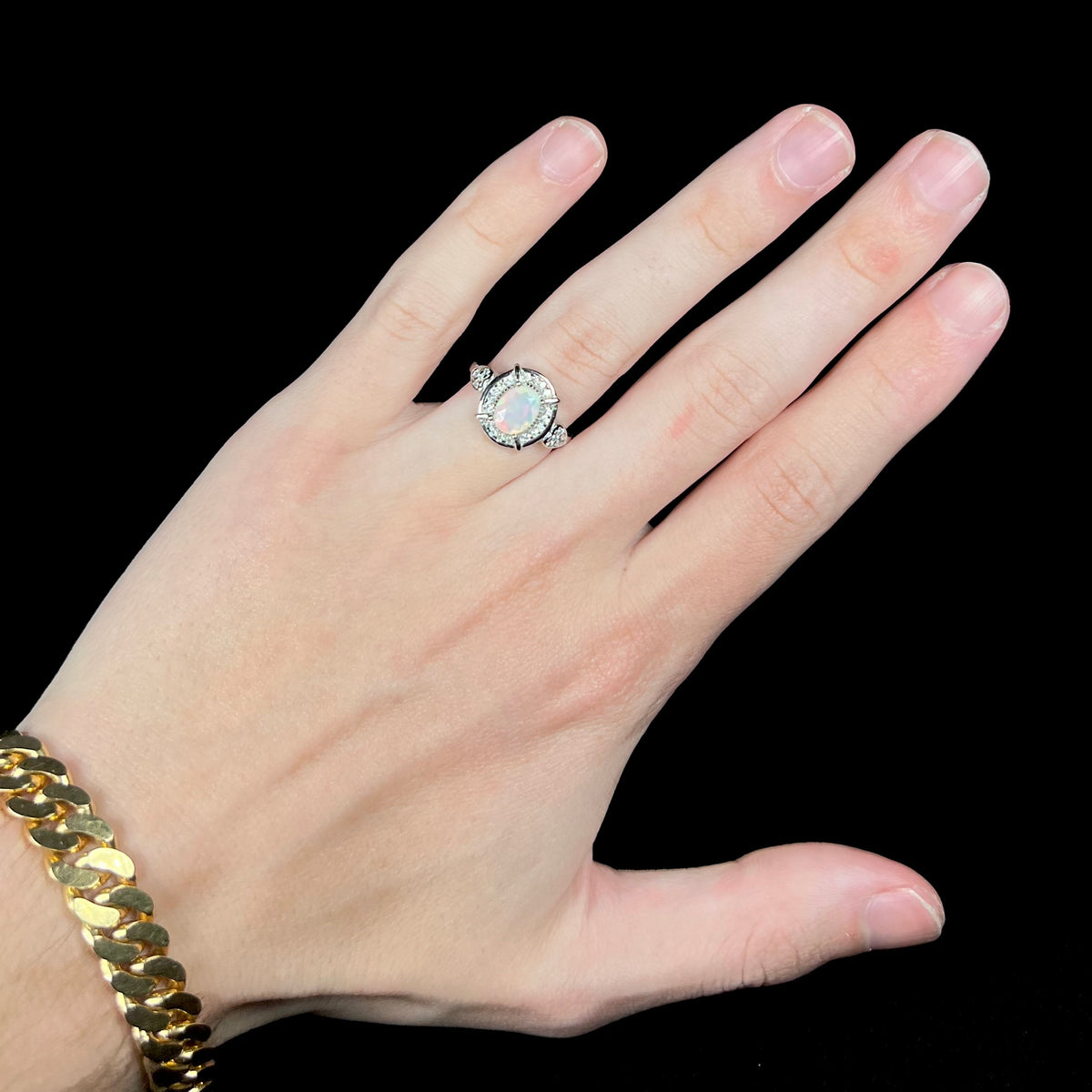 Hand wearing women's silver Ethiopian opal and CZ halo design ring
