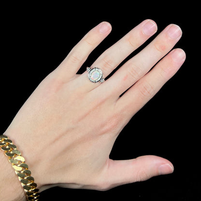 Hand wearing women's silver Ethiopian opal and CZ halo design ring