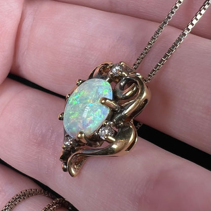 A women's synthetic opal and CZ necklace with a gold-tone Victorian style setting, shown close-up from an angle on fingers.