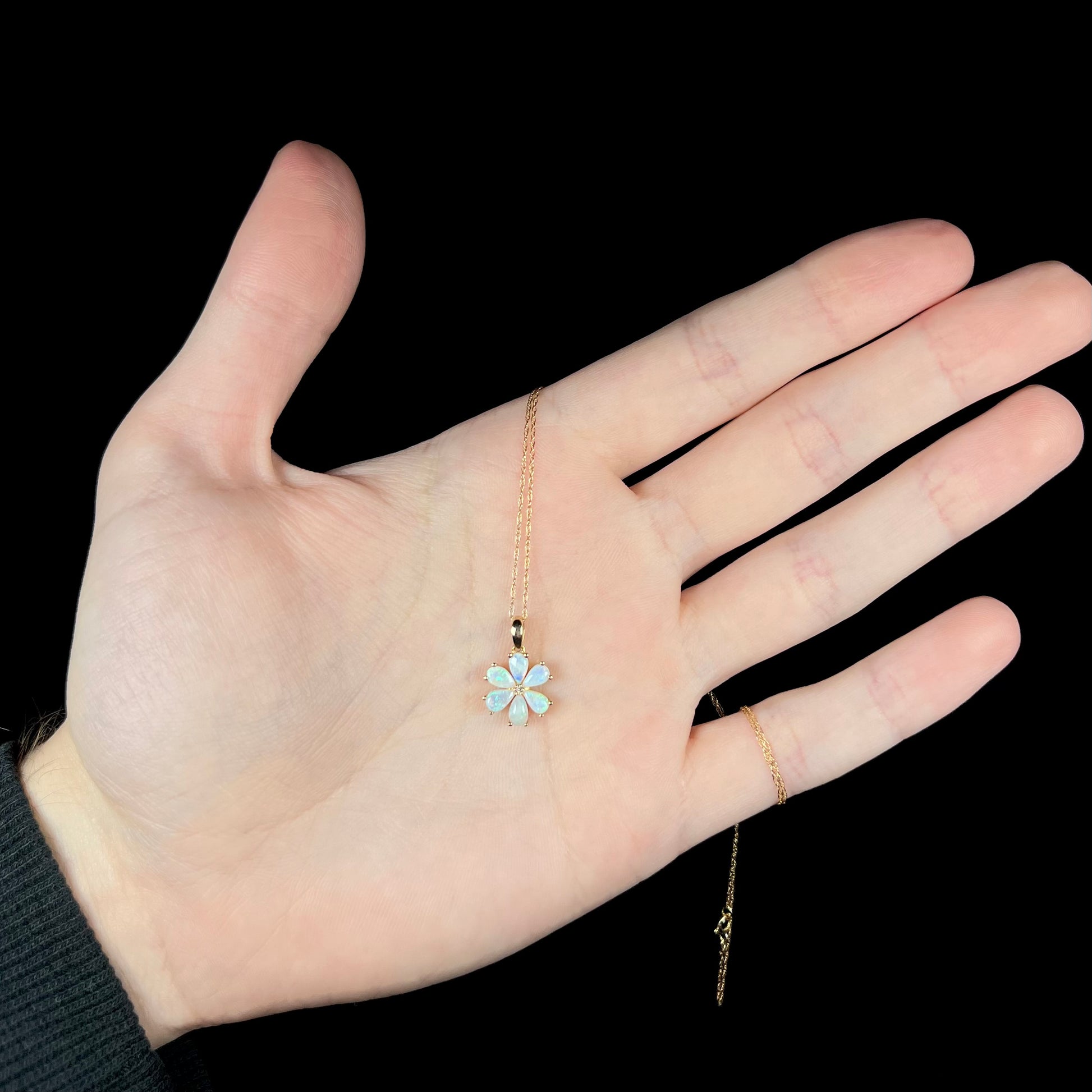 Hand holding women's opal and diamond flower necklace with gold chain