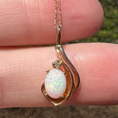 Close-up of women's opal and diamond pendant in 14k gold, held on top of fingers in direct sunlight