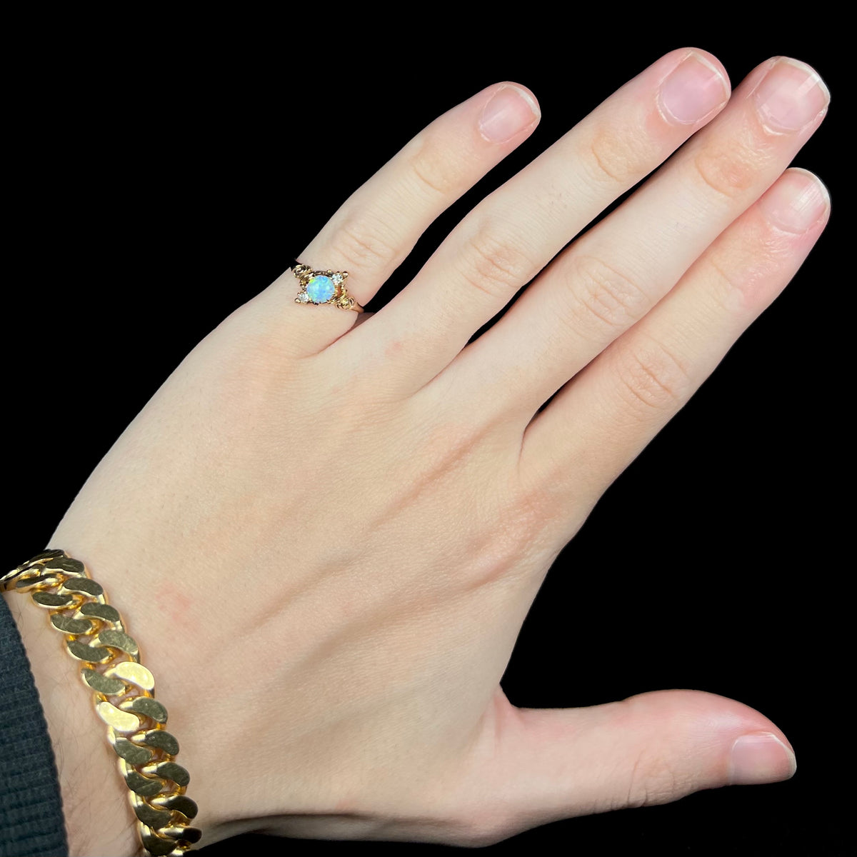 Hand wearing women's antique 10k gold Art Nouveau opal and diamond pinky ring under cool LED studio light
