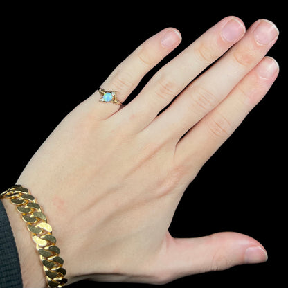 Hand wearing women's antique 10k gold Art Nouveau opal and diamond pinky ring under cool LED studio light